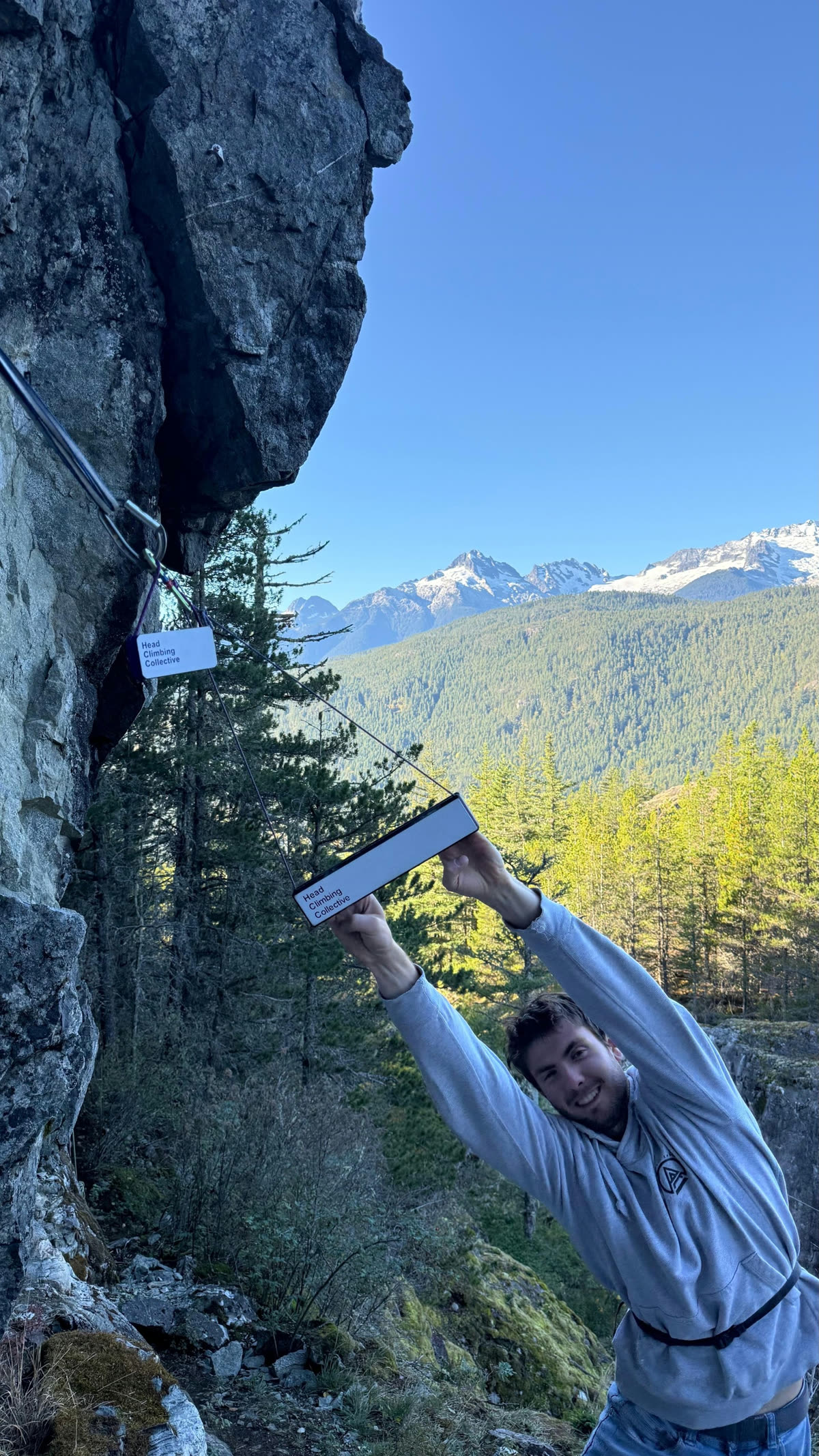 Smiling climber pulling down on a DriftBoard hung from a quickdraw on a Squamish granite wall