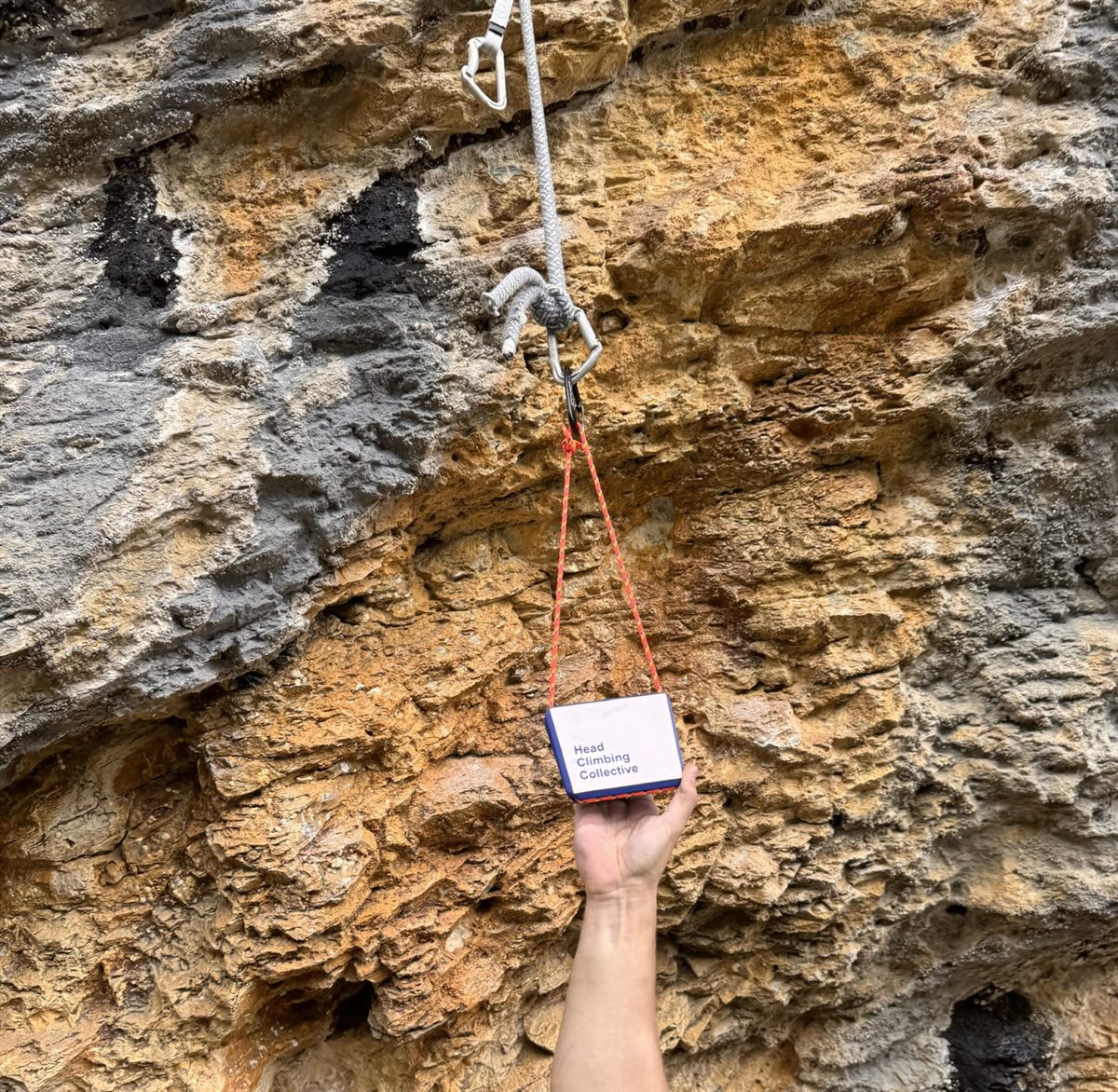 Hand pulling on a TriEdge Crimp Block clipped to a bolt on orange limestone