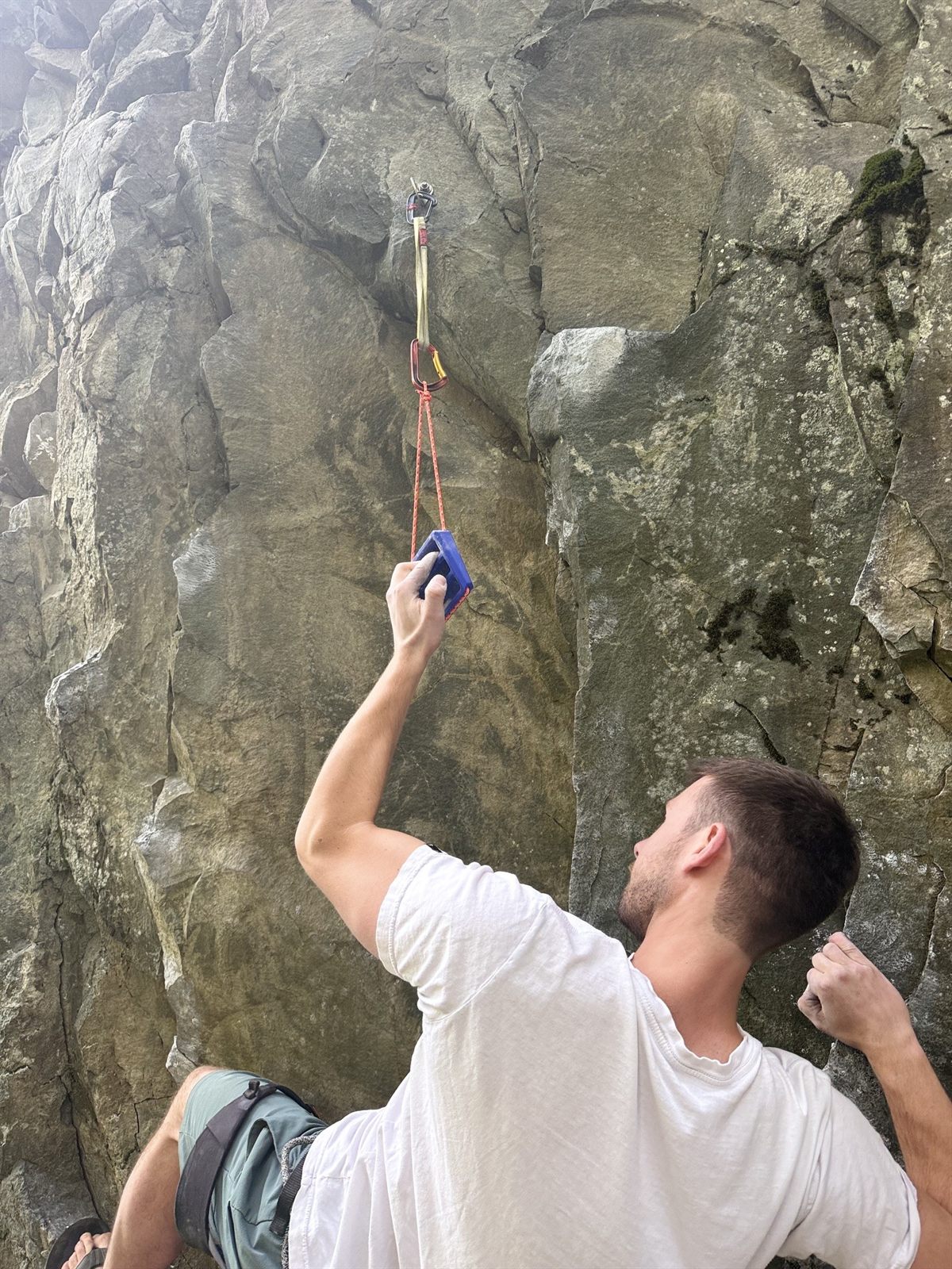 Climber warming up on a blue TriEdge Crimp Block hung from a quickdraw at the base of a grey rock wall