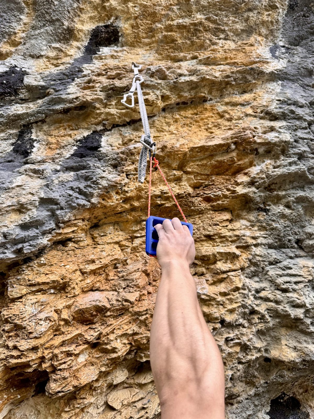 Hand gripping a blue TriEdge Crimp Block hung from a quickdraw on a limestone wall