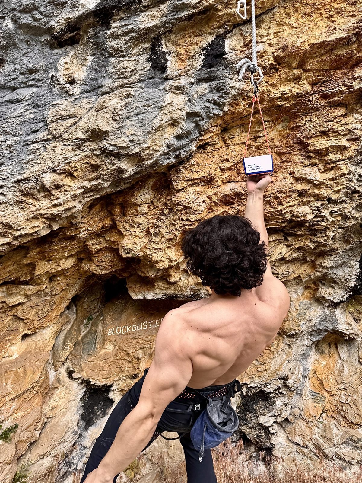 Climber reaching up to a TriEdge Crimp Block hung from a bolt on an orange limestone overhang